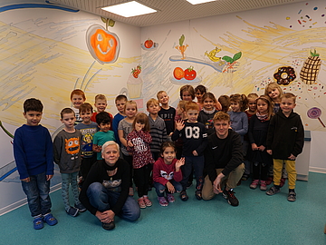 Das Bild zeigt die Kinder vor den bunt bemalten Wänden